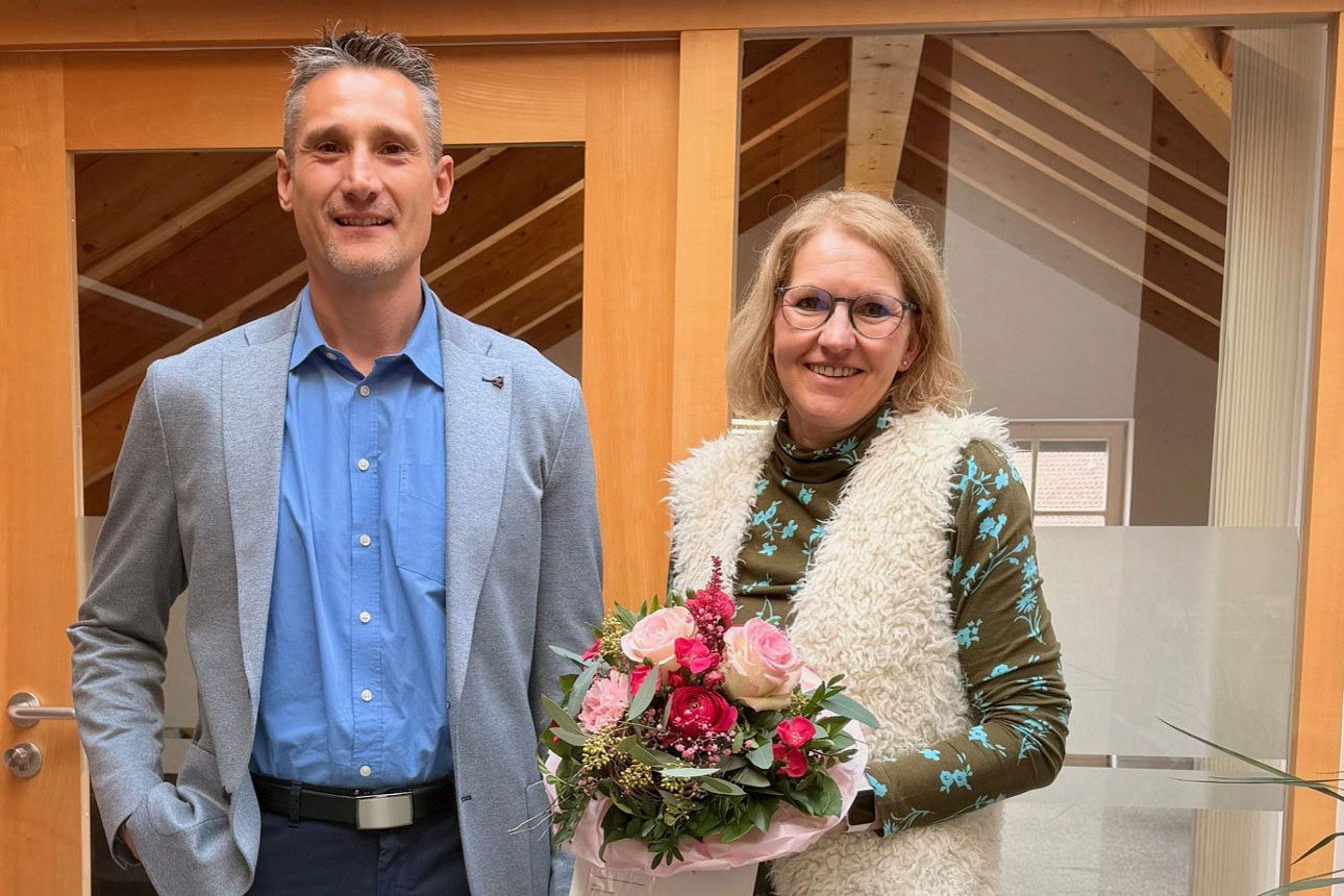 Ein Mann und eine Frau stehen nebeneinander, die Frau hält einen Blumenstrauß in den Händen, beide lächeln in die Kamera