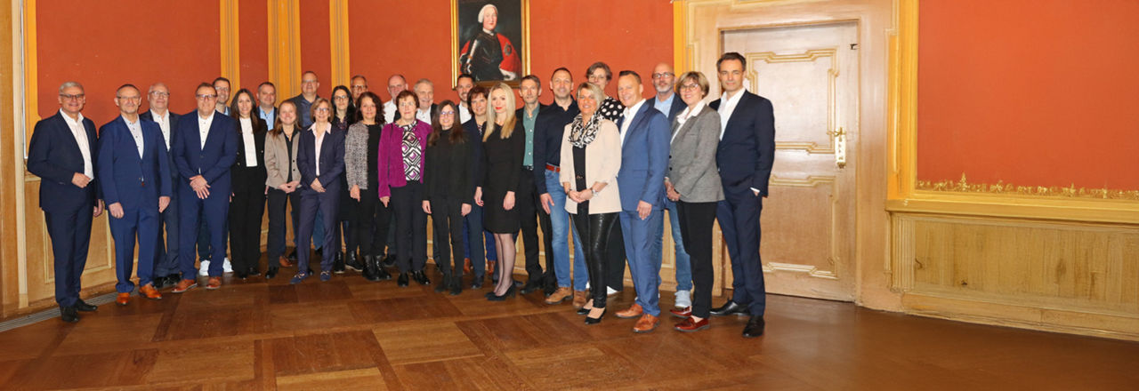 Das Bild zeigt die Ehrung langjähriger Mitarbeiter der VR Bank. Stolze Jubilare stehen und lächeln, umgeben von Kollegen und Vorgesetzten.