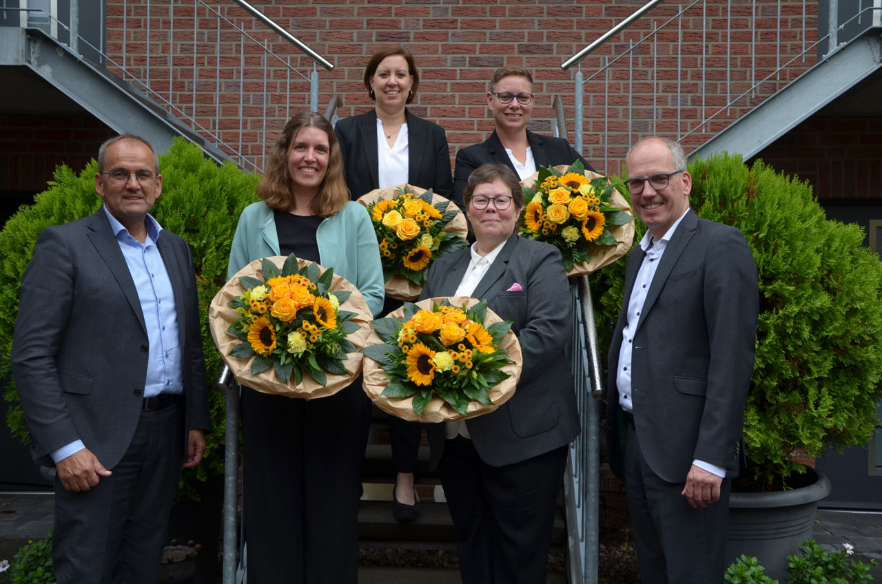 Vier Frauen mit Blumensträußen in der Hand und zwei Männer stehen auf einer Treppe