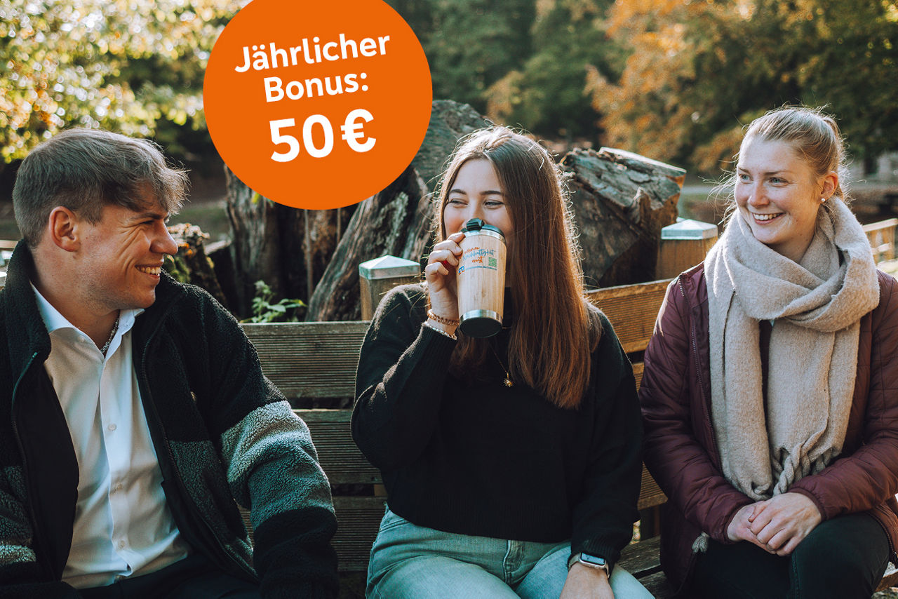 Drei junge Manschen sitzen auf einer Bank und lächeln einander zu