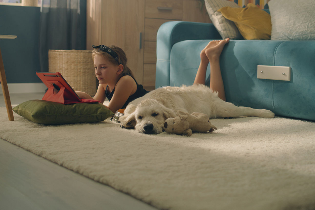 Mädchen liegt mit Laptop auf einem Teppich.