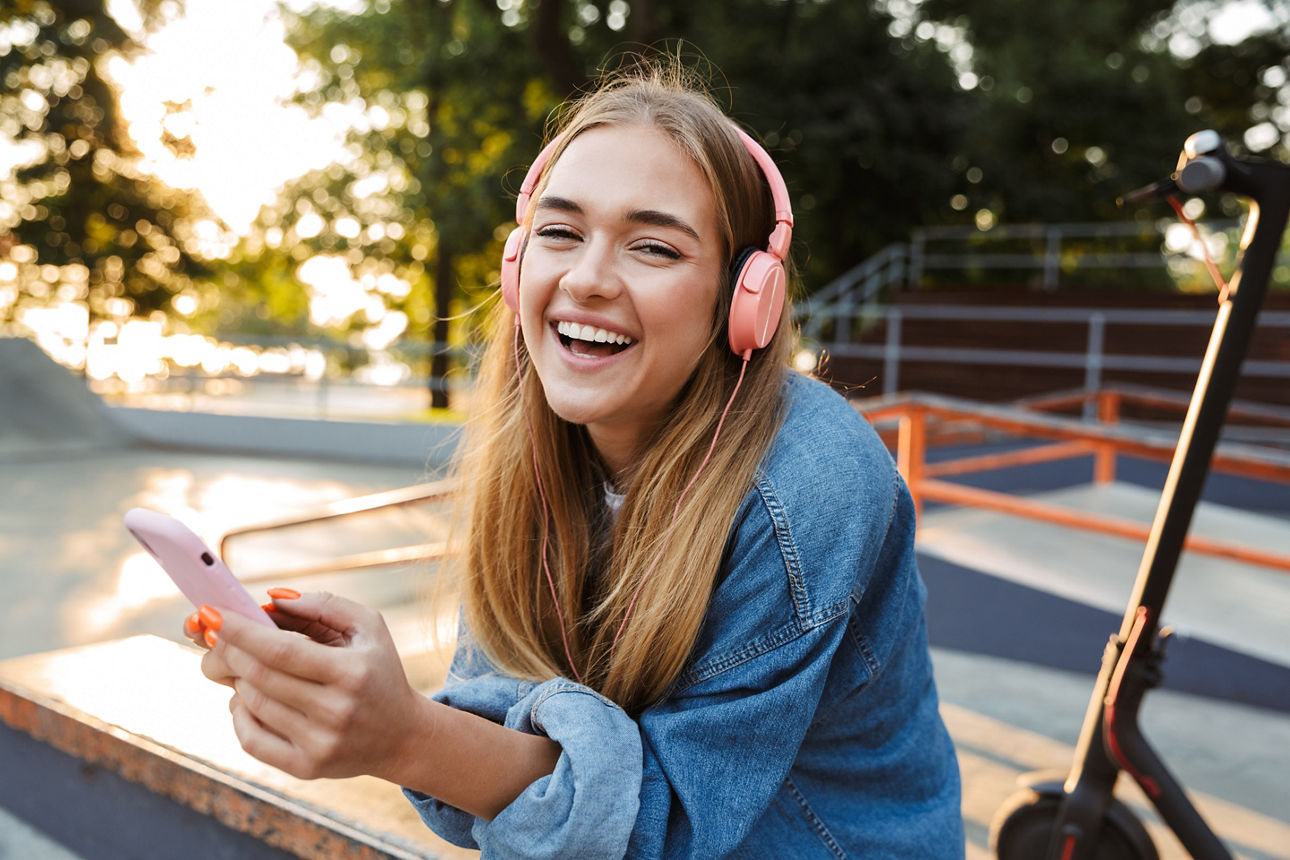Eine Person, die mit pinken Kopfhörern und einem Smartphone in der Hand auf einer Skatepark-Rampe sitzt.