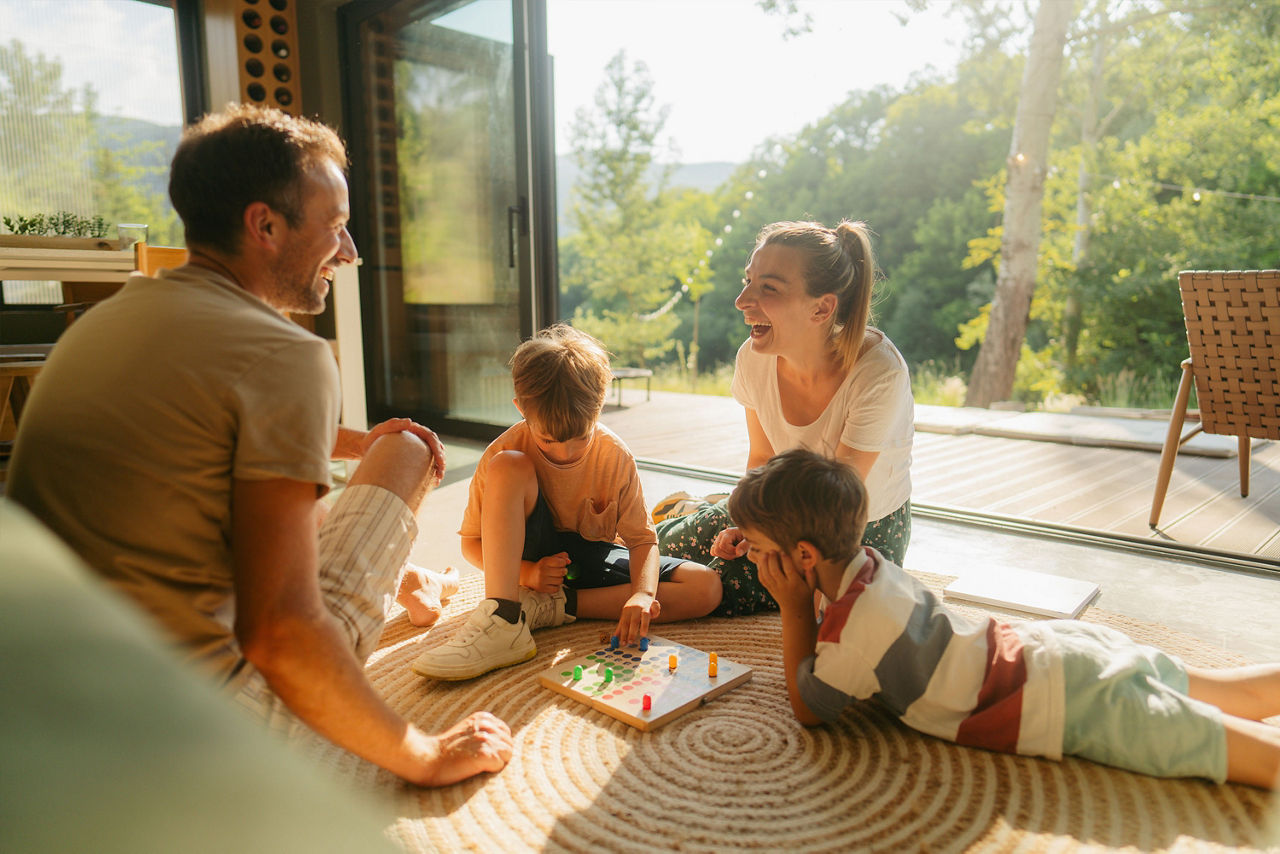 Familie spielt im Wohnzimmer gemeinsam ein Brettspiel auf dem Boden.