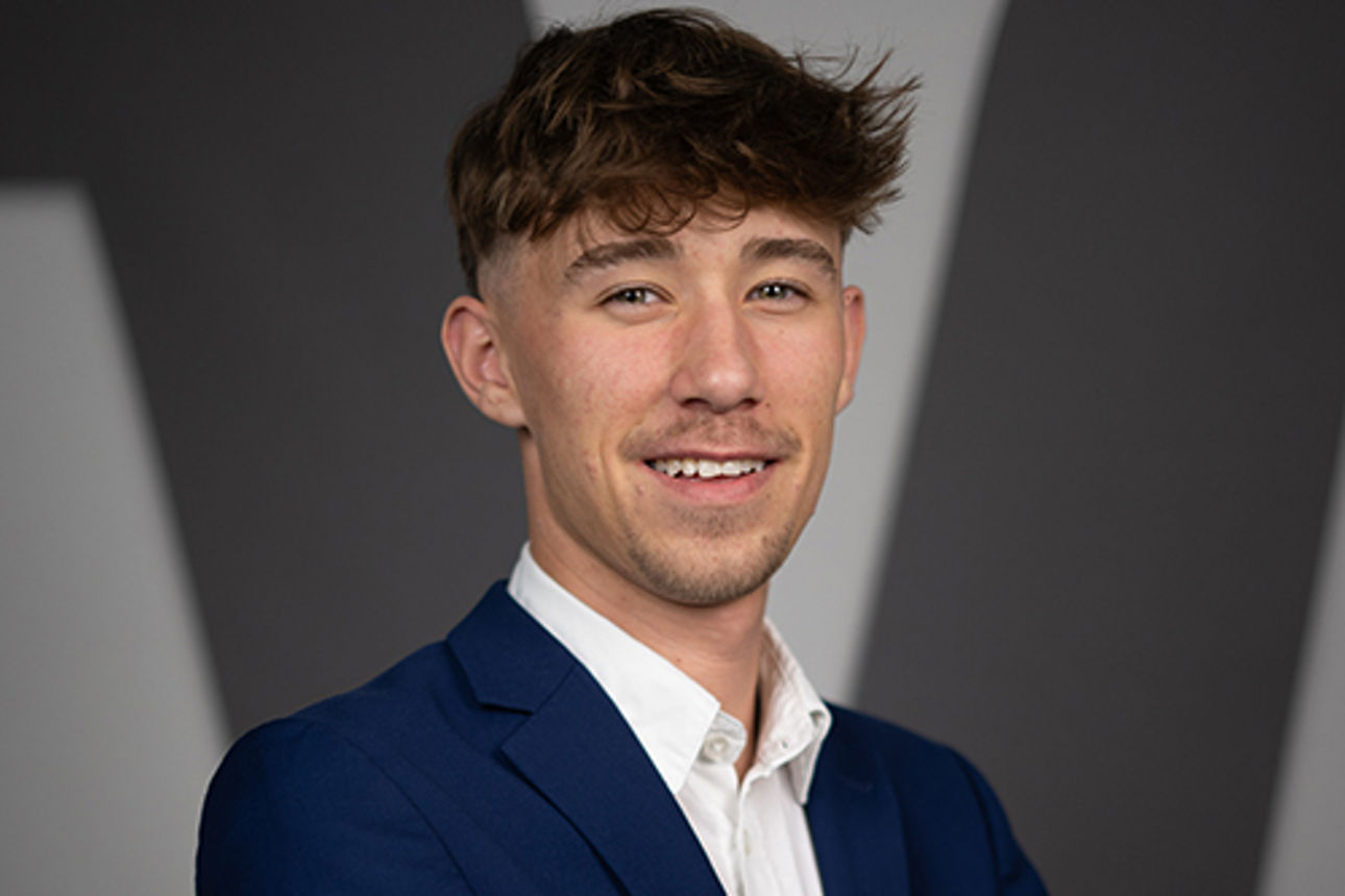 Eine junger Mann steht mit verschränkten Armen vor dem Lodo der Volksbanken-Raiffeisenbanken.