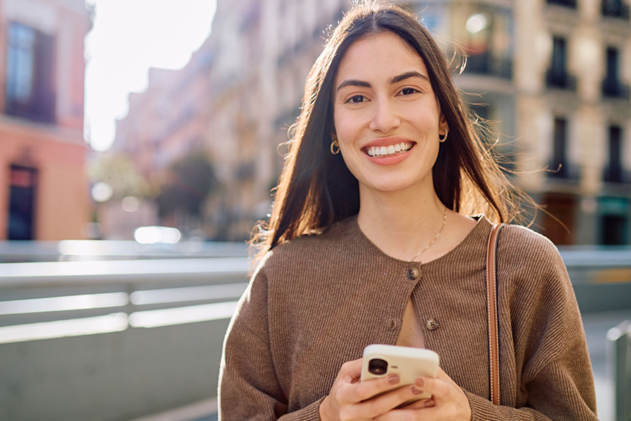 Eine lächelnde junge Frau mit ihrem Handy in der Hand