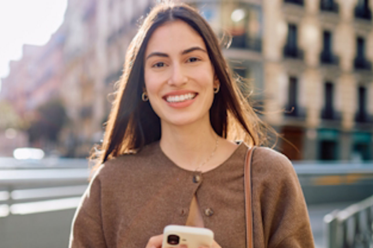 Eine lächelnde junge Frau mit ihrem Handy in der Hand