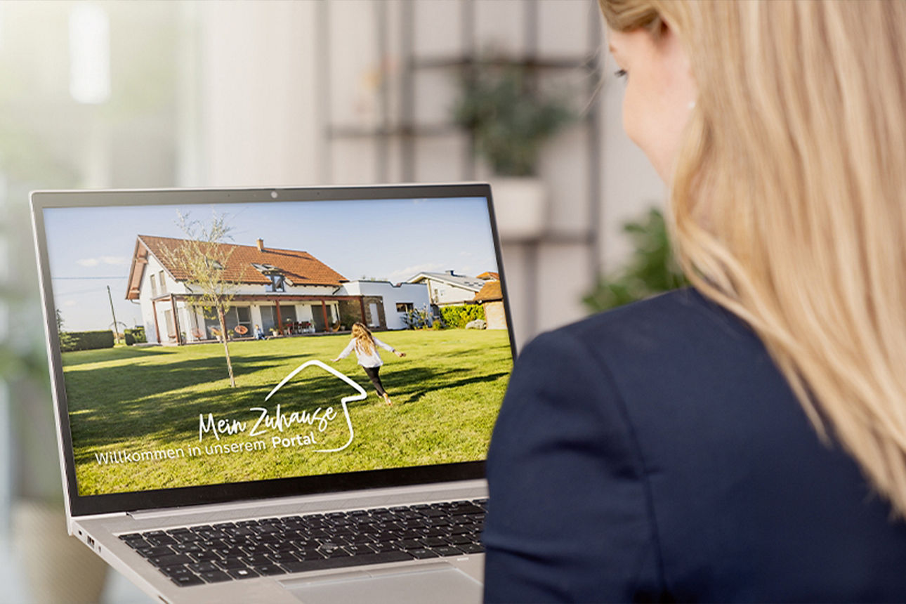 Junge Frau hält Laptop mit MeinZuhausePortal auf dem Display in der Hand