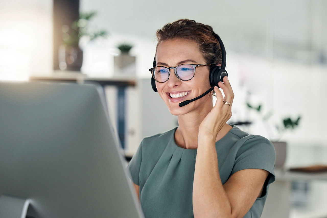 Junge Frau sitzt am PC und telefoniert über ein Headset