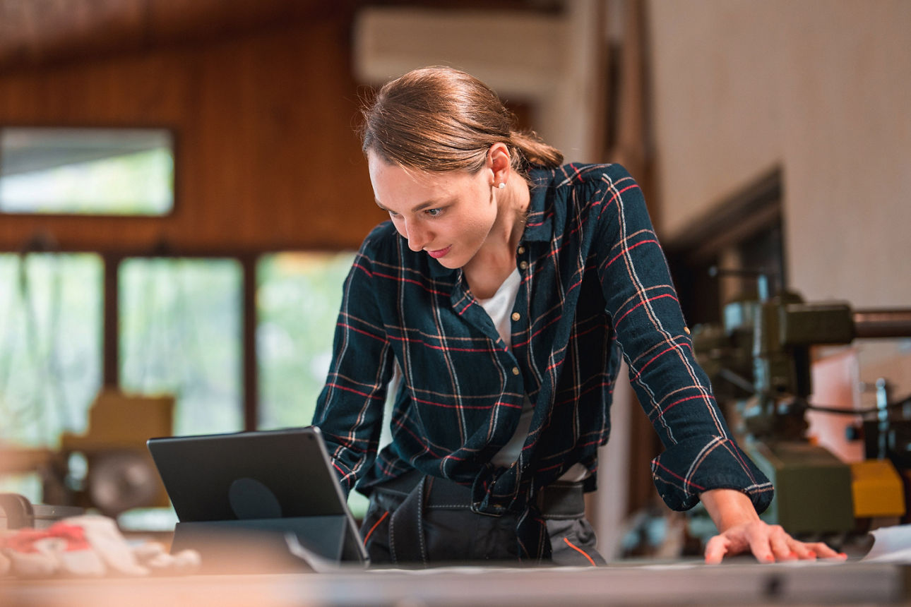 Junge Frau steht in einer Werkstatt und schaut in ein Tablet