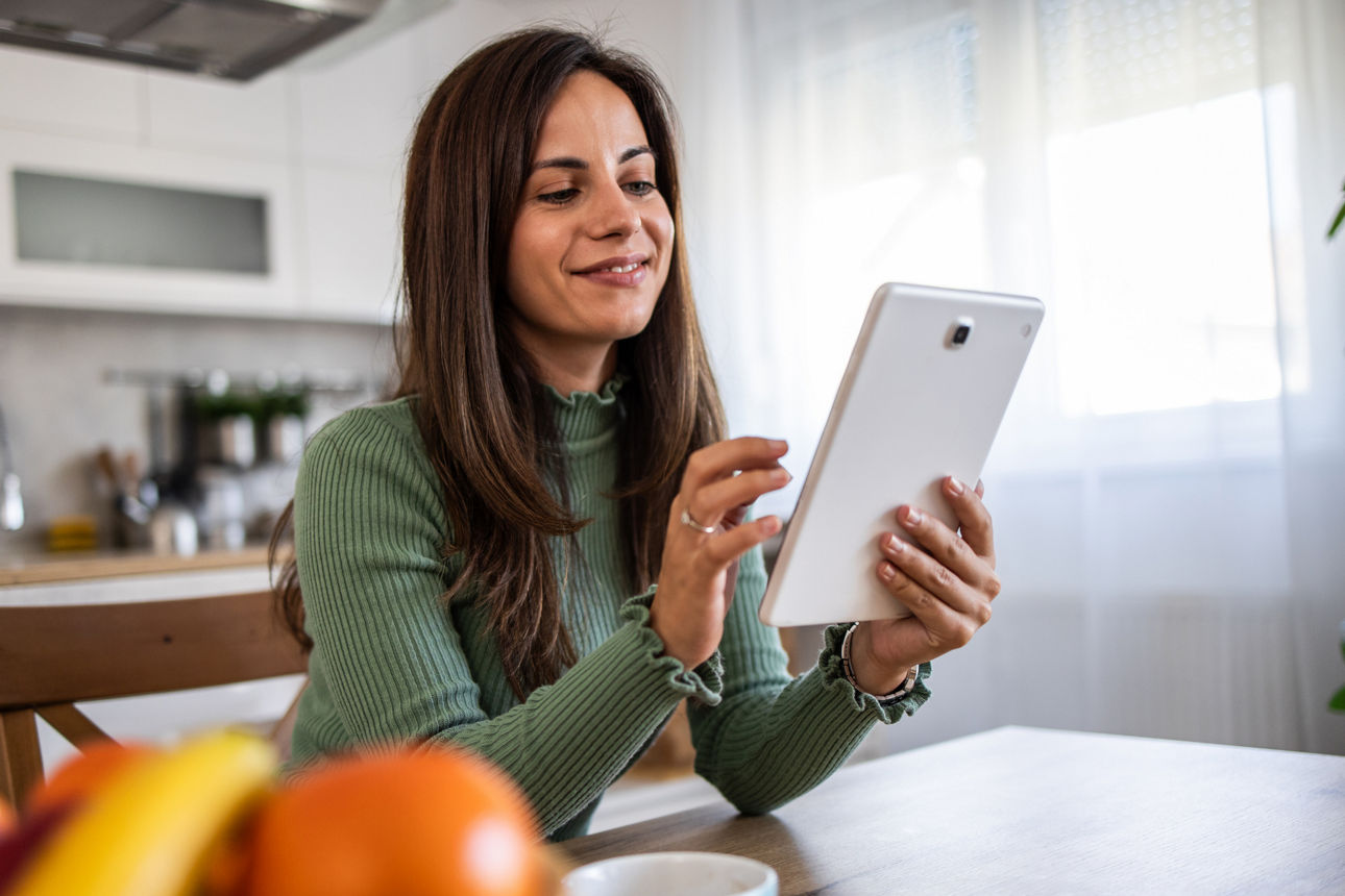 Lächelnde Frau, die Kaffee trinkt und ein Tablet benutzt