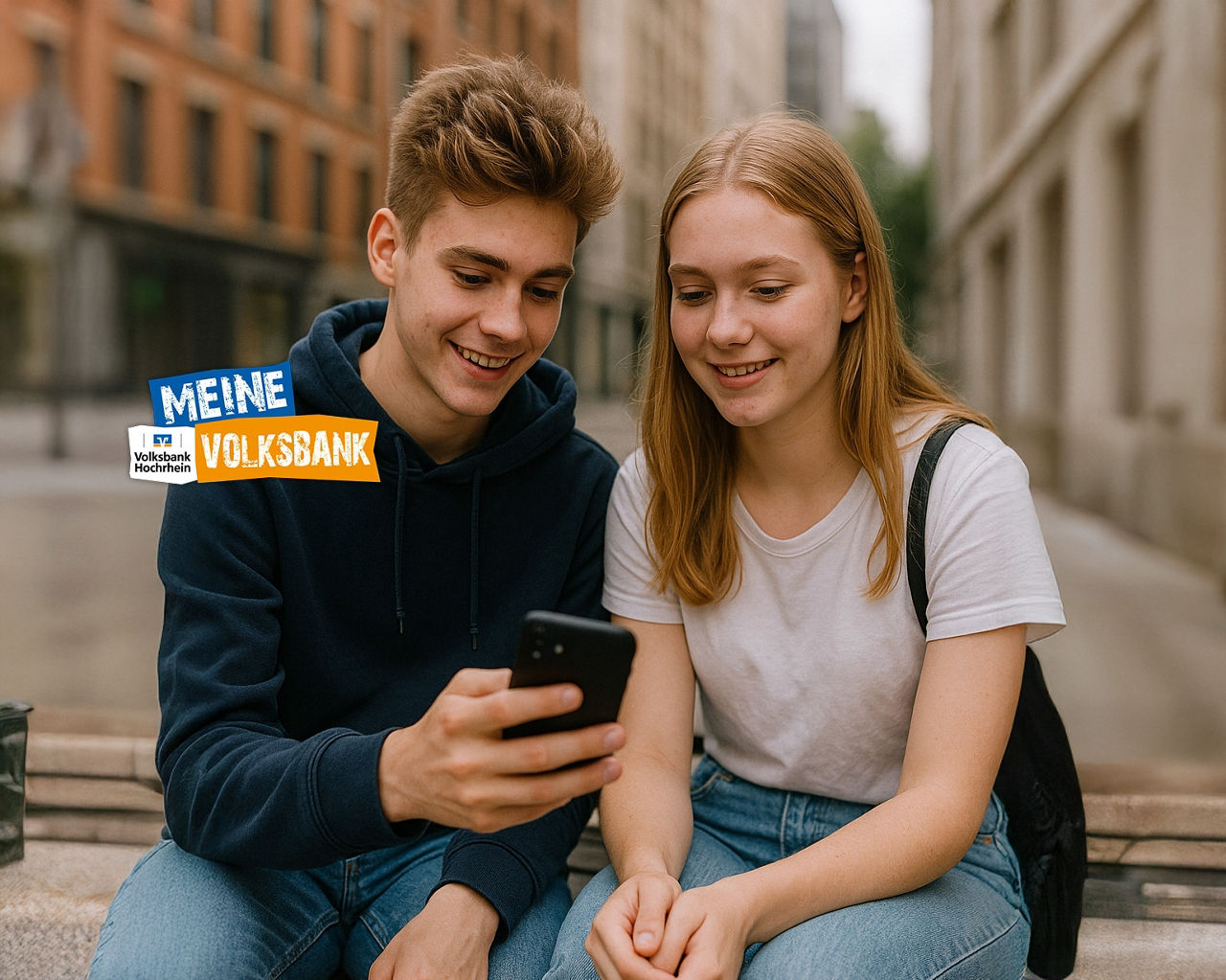 Zwei Jugendliche sitzen auf einer Bank. Der junge Mann hält ein Smartphone in der Hand. Beide schauen auf das Smartphone.