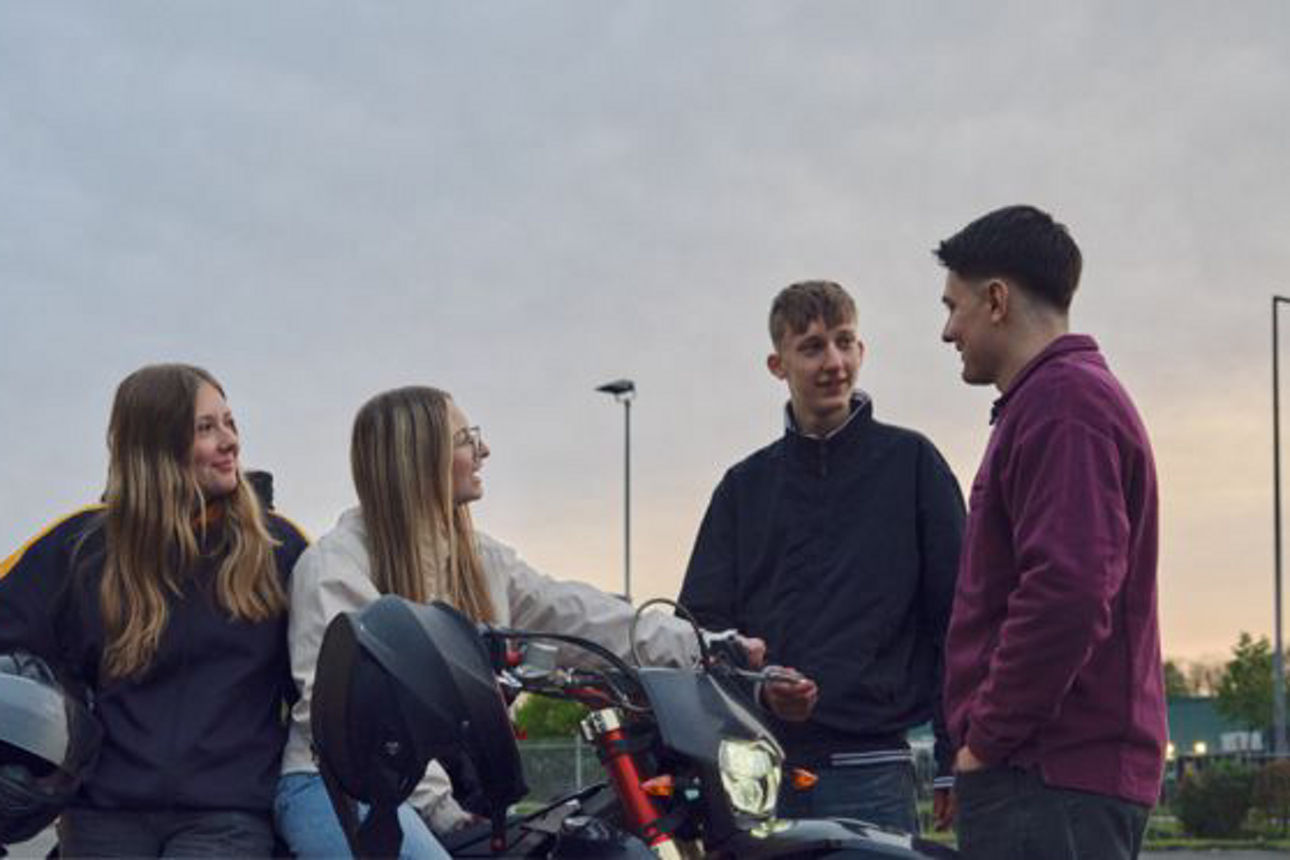 Junge Leute mit Moped stehen zusammen und reden