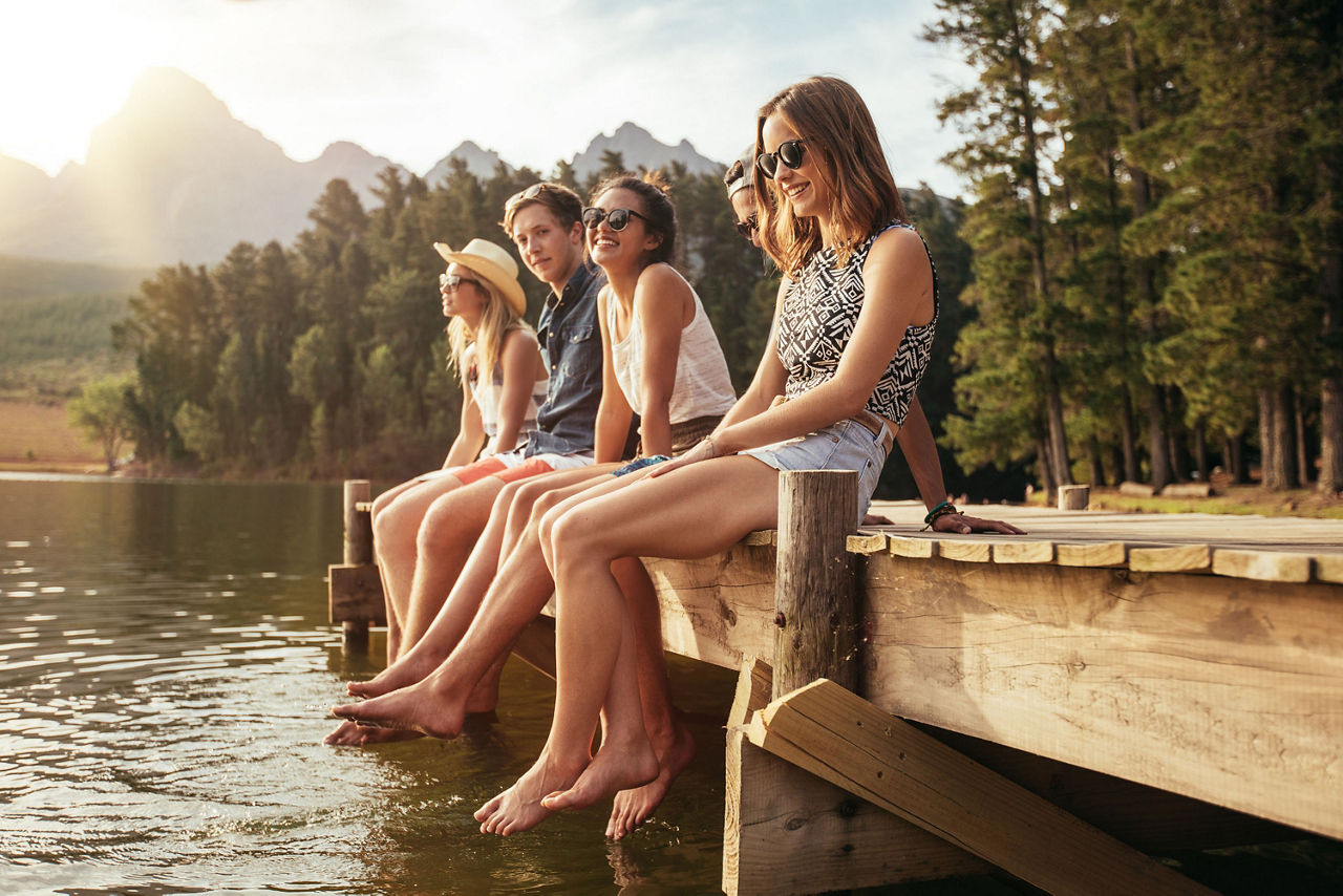 5 Jugendliche sitzen nebeneinander auf einem Steg am See
