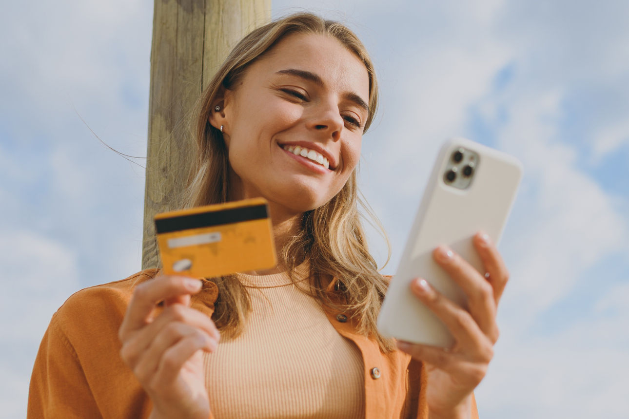 Junge Frau lächelt mit einer Kreditkarte und einem Handy in der Hand