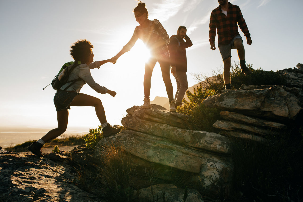 Gruppe junger Menschen wandert bei Sonnenuntergang, eine Person hilft einer anderen über Felsen hinauf