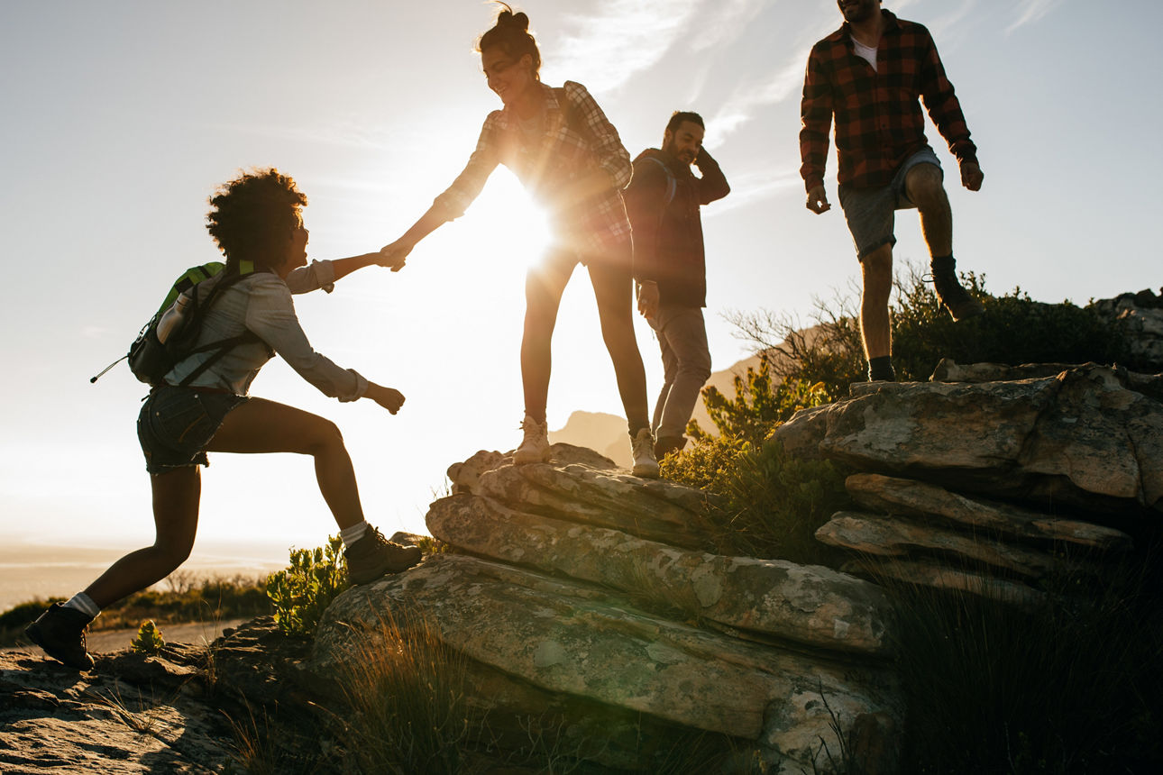 Gruppe junger Menschen wandert bei Sonnenuntergang, eine Person hilft einer anderen über Felsen hinauf