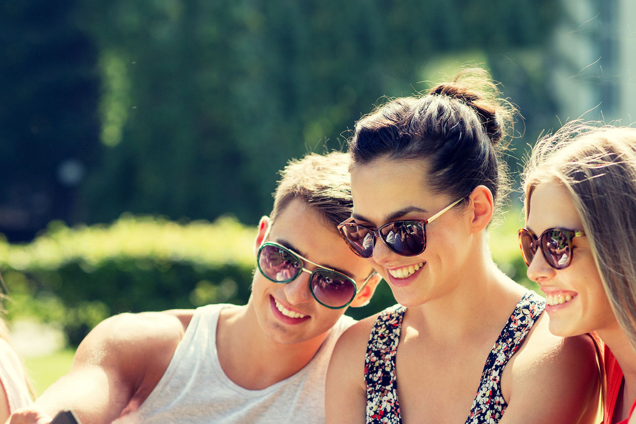 lachende Freunde sitzen mit ihrem Smartphone im Park
