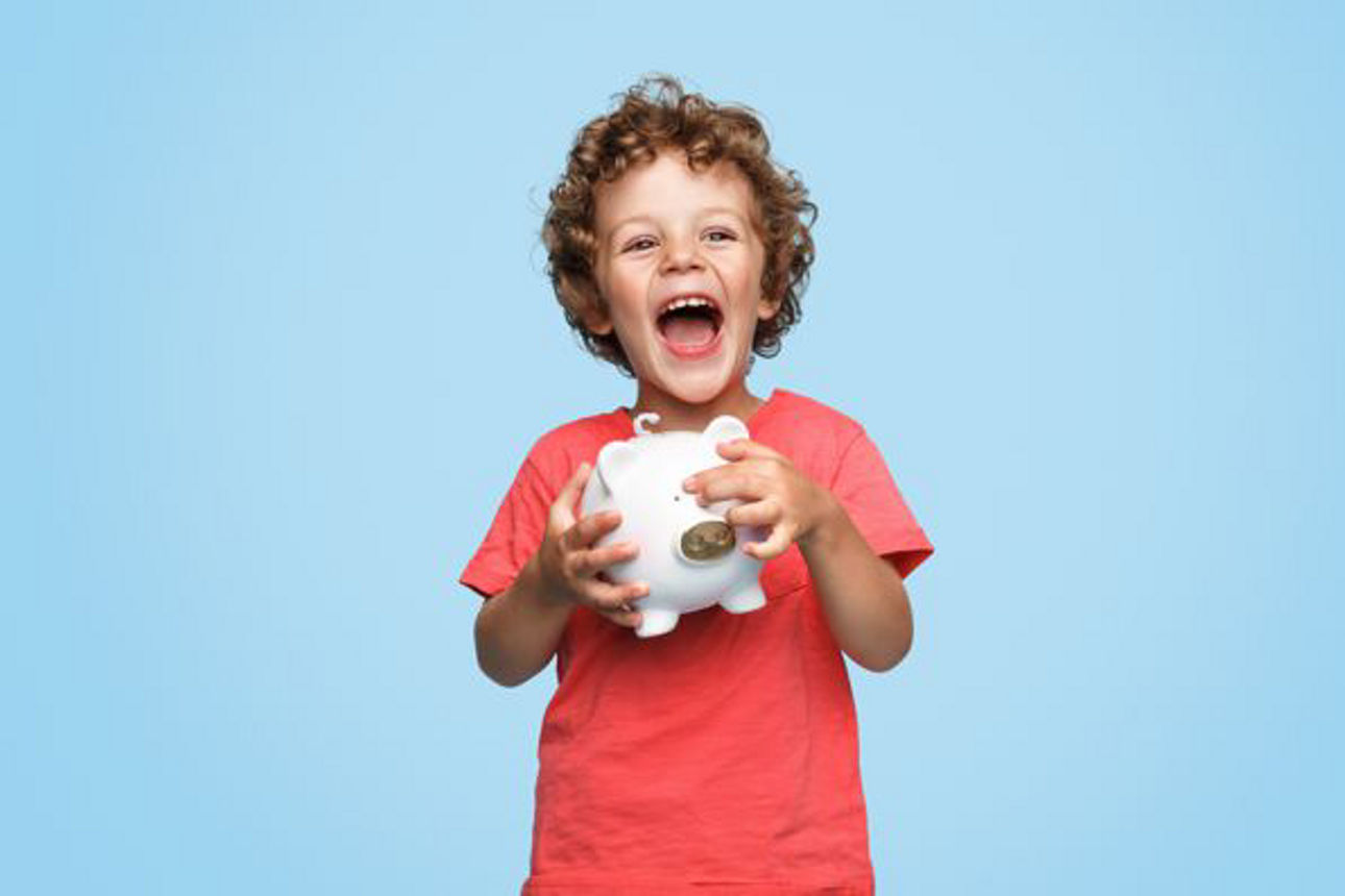 Cute little boy with piggy bank laughing and looking at camera while standing on blue background