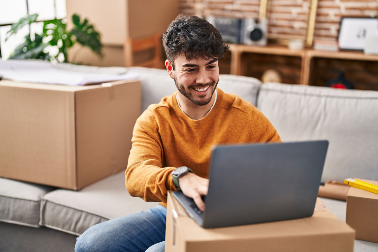 junger Mann mit Laptop auf Umzugskarton