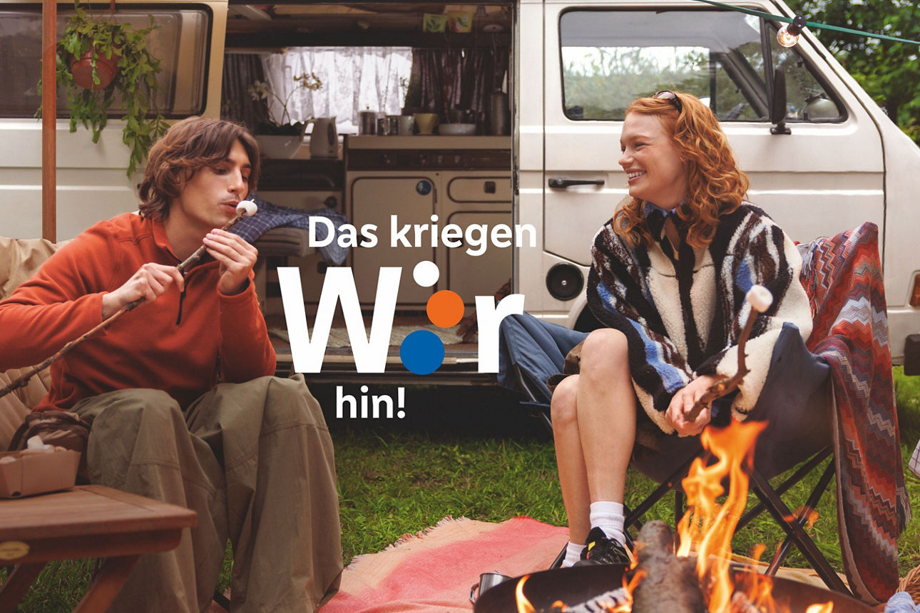 Ein junges Paar röstet Marshmellows vor einem weißen VW-Bus