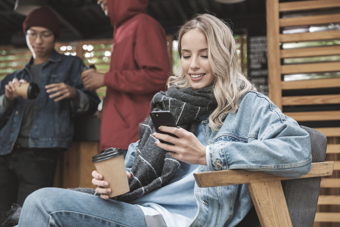 Junge Frau mit Handy, lächelnd, vor einem Mann, vor einem hellen Hintergrund