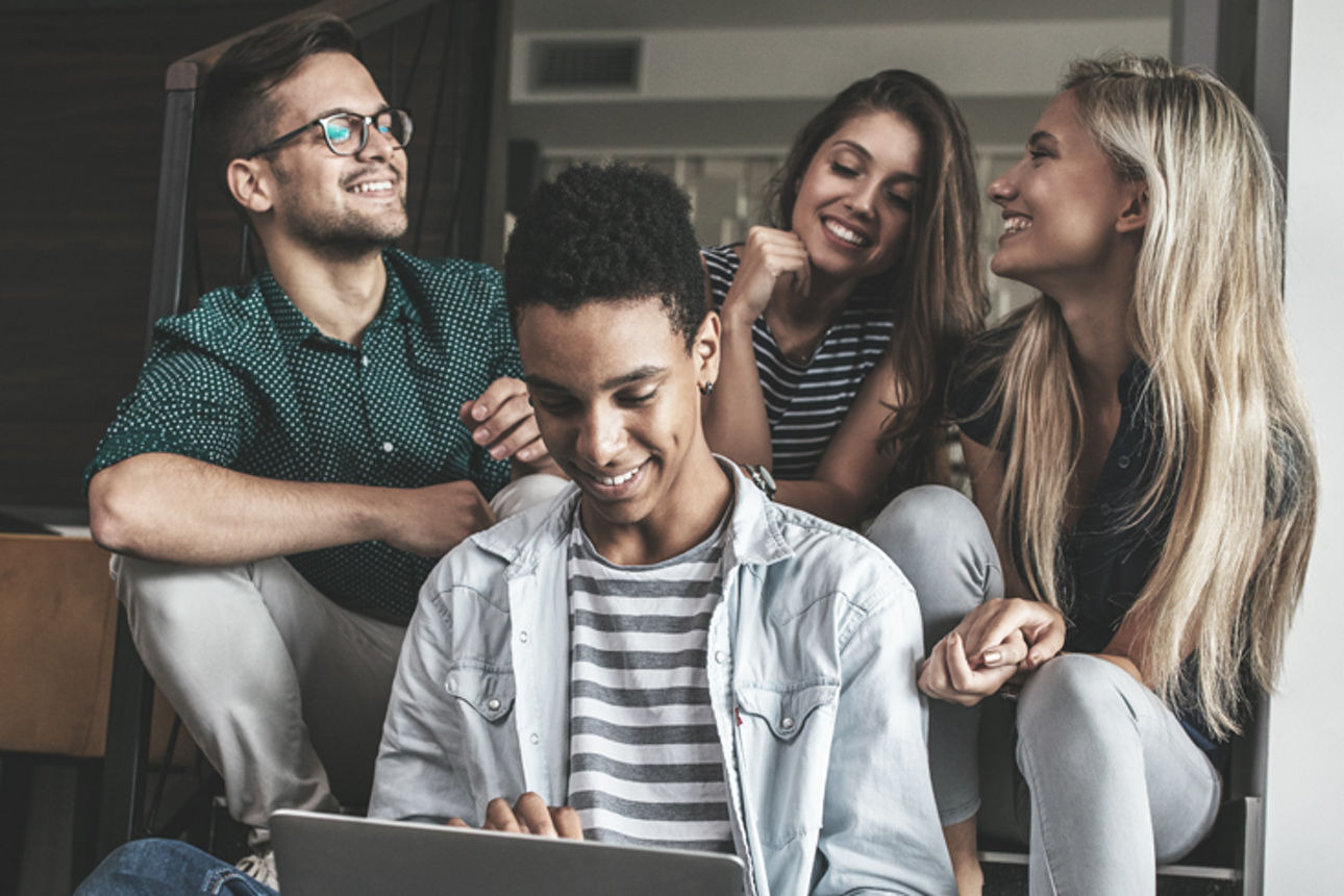 Eine Gruppe von vier Freunden sitzt in einer lockeren Umgebung und lächelt