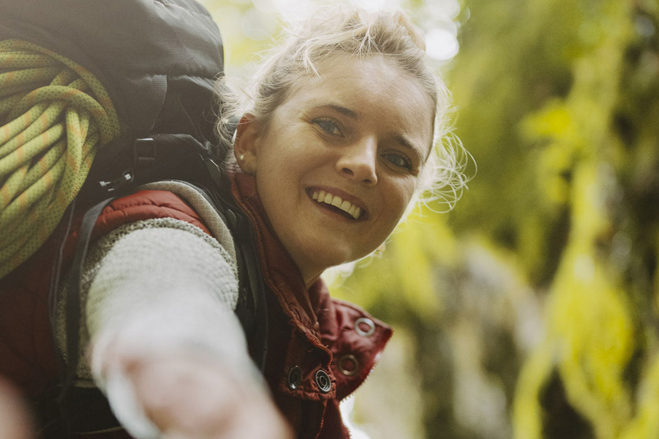 Junge Frau klettert in den Bergen und reicht dem Betrachter die Hand