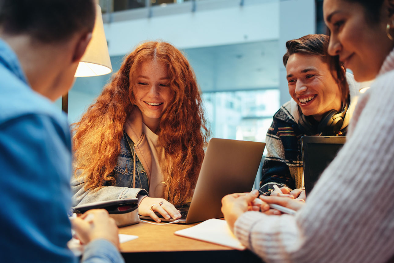 Group of young students in library discussing assignments. College classmates doing project together in library.