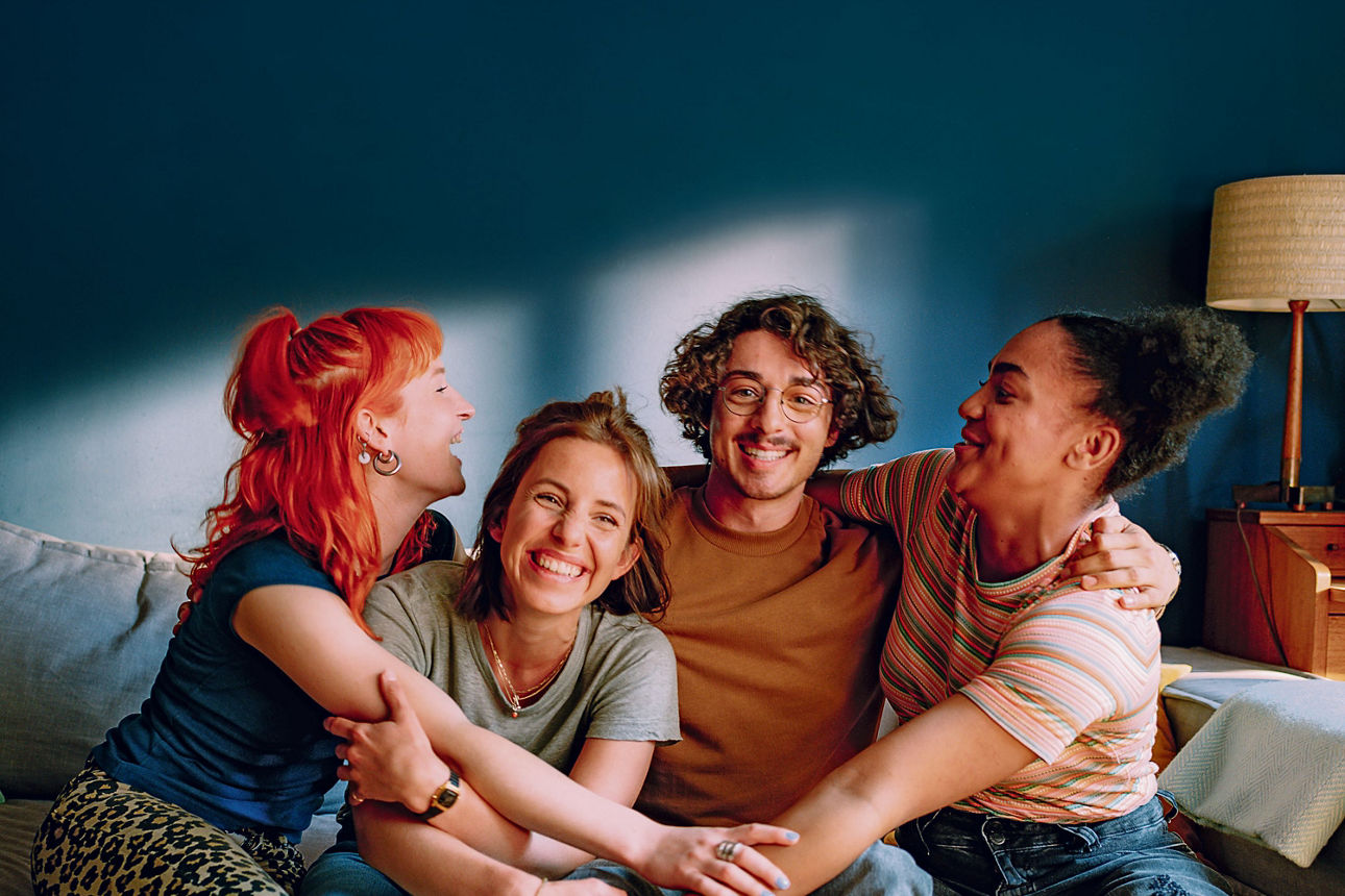 4 Freunde zusamen auf dem Sofa lachend und halten zusammen
