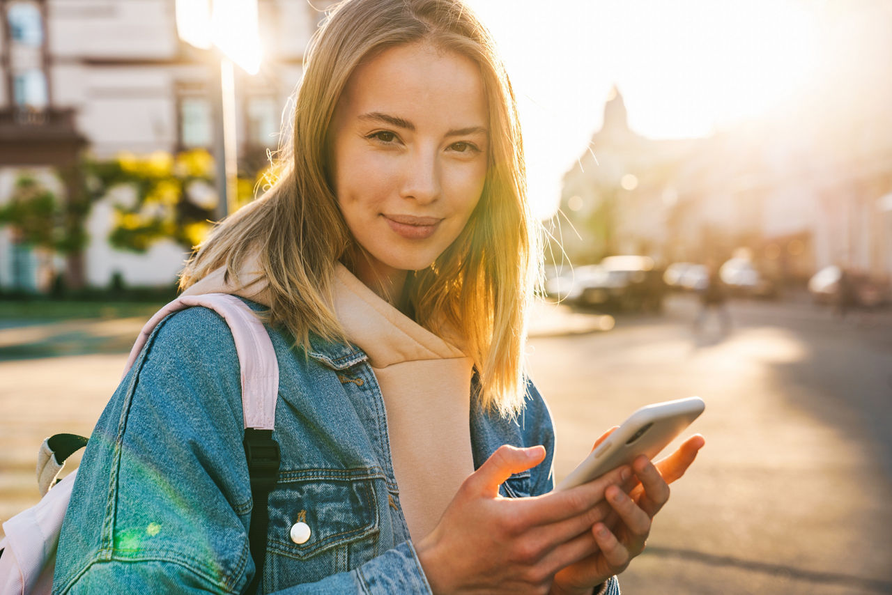 Jugendliches Mädchen mit einem Handy in der Hand läuft lächelnd durch die Straße