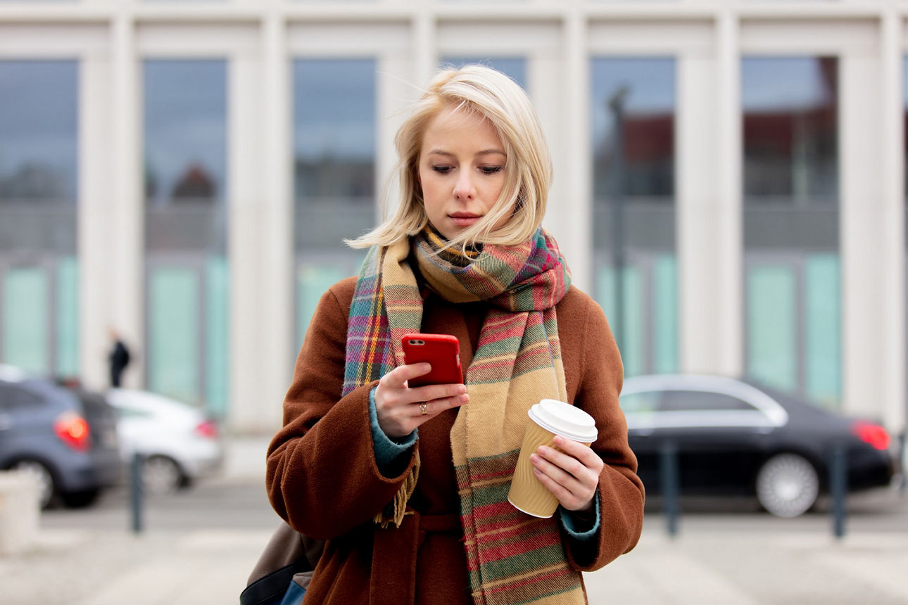 Schöne blonde Frau mit einer Tasse Kaffee mit dem Handy