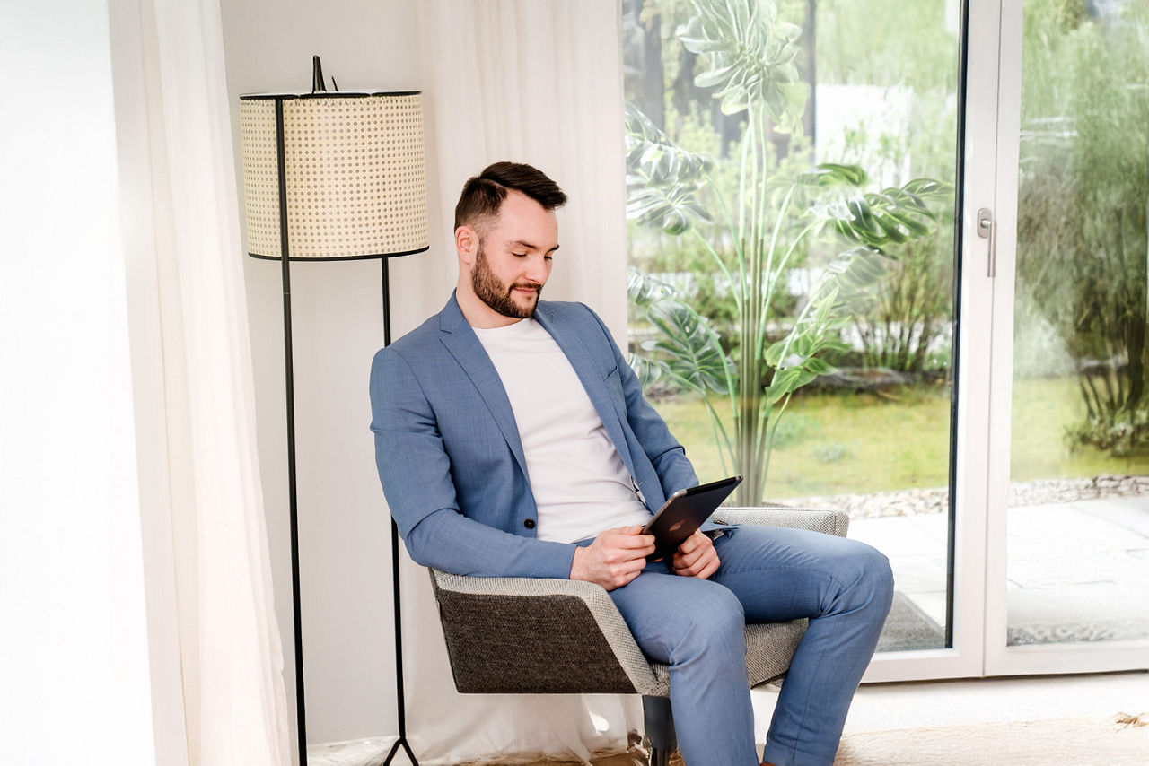 Junger Mann mit Tablet in der Hand sitzt in einem Sessel