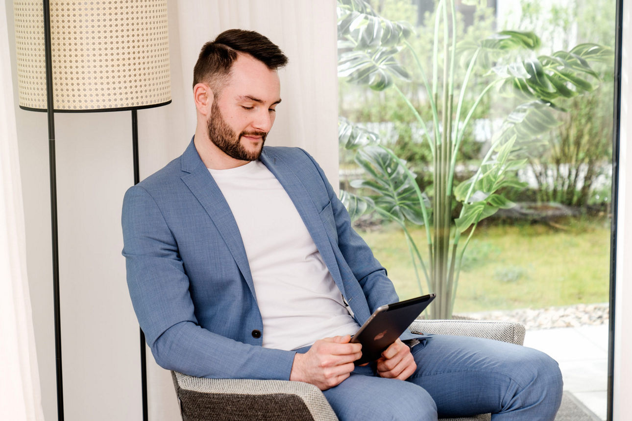 Junger Mann mit Tablet in der Hand sitzt in einem Sessel