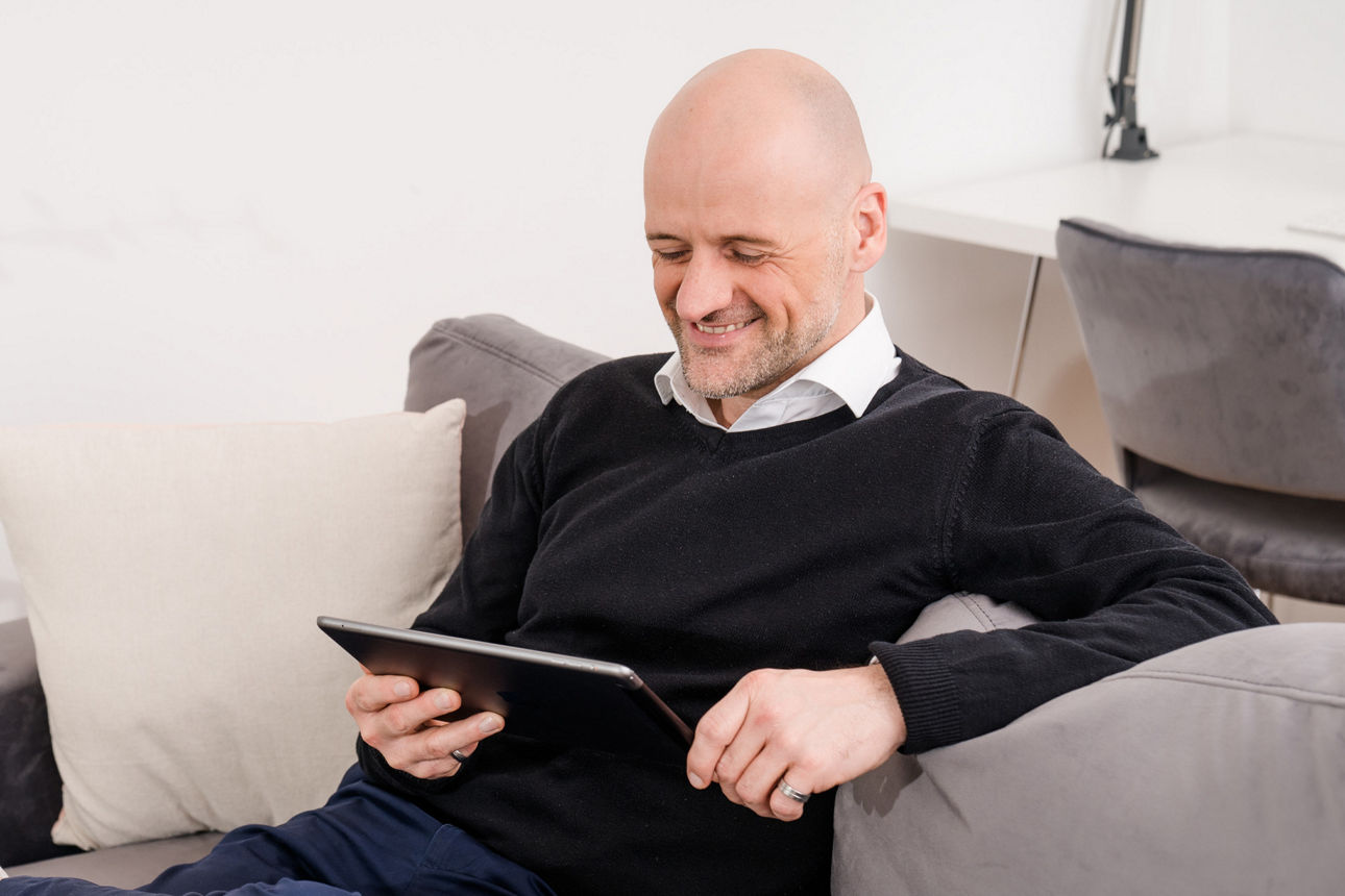 Junger Mann sitzt auf dem Sofa und schaut in ein Tablet