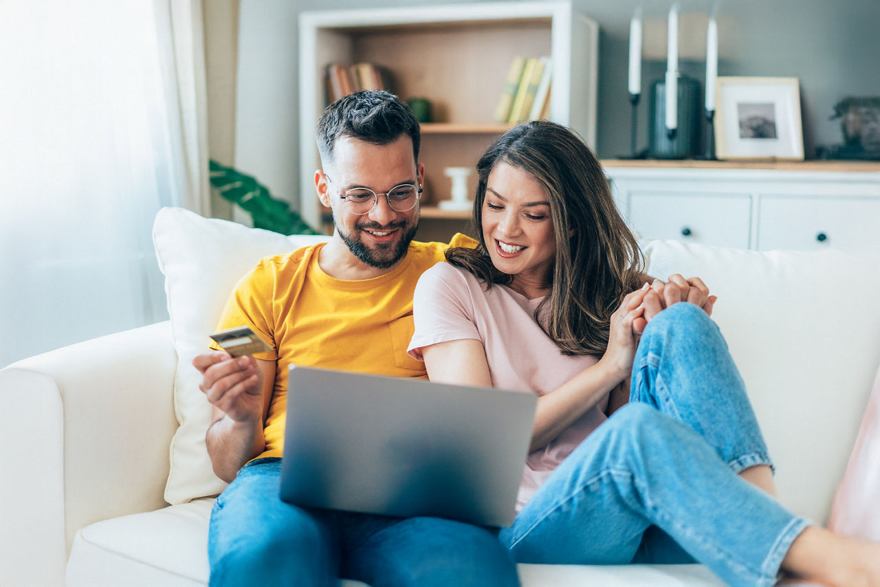 Junges Paar sitzt mit dem Laptop auf dem Sofa und recherchiert im Internet