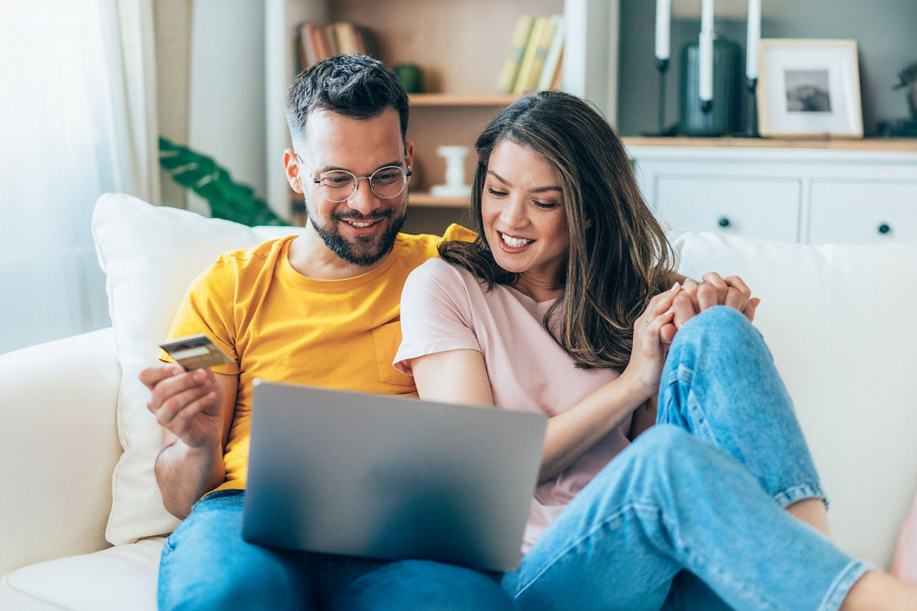 Junges Paar sitzt mit dem Laptop auf dem Sofa und recherchiert im Internet