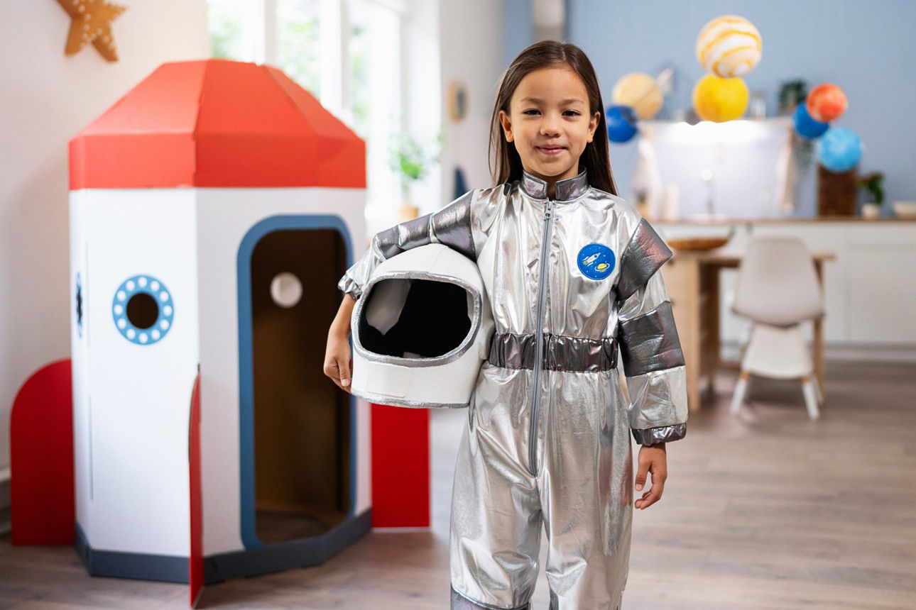 Junges Mädchen im Astronautenanzug steht vor Papprakete