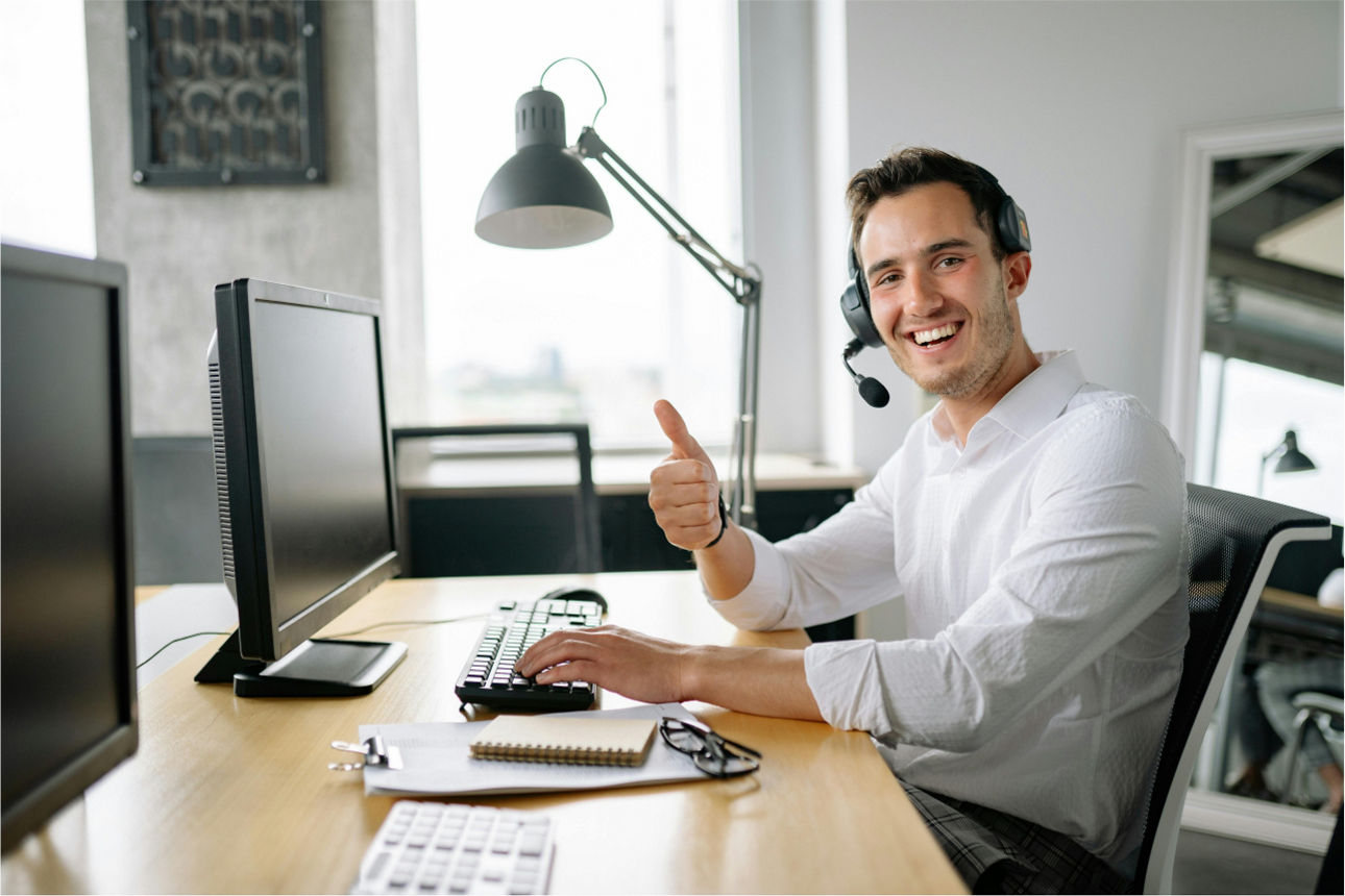 Ein Mann sitzt vor zwei PC-Monitoren, trägt ein Headset und zeigt einen Daumen nach oben.