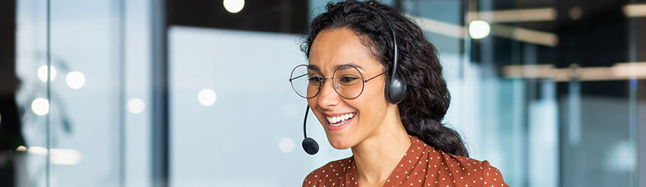 Eine Frau arbeitet in einem modernen Büro, lächelt und spricht remote über ihren Laptop und ein Headset