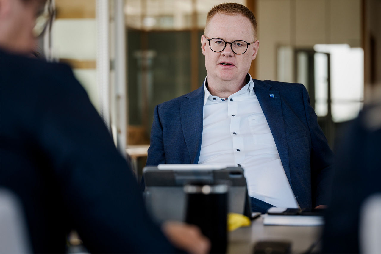 Eine Person sitzt an einem Besprechungstisch und spricht mit anderen