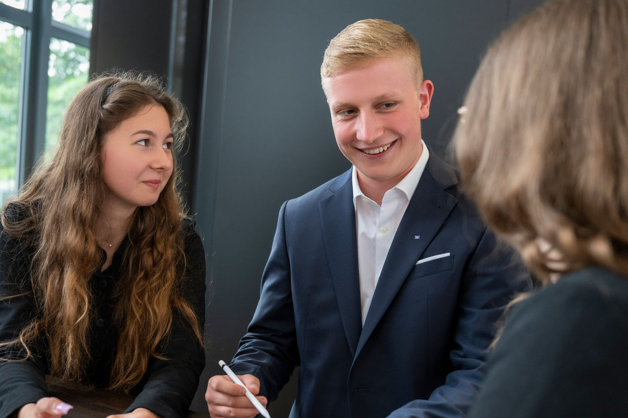 Zwei junge Frauen schauen einen jungen Mann an, der einen Anzug trägt.