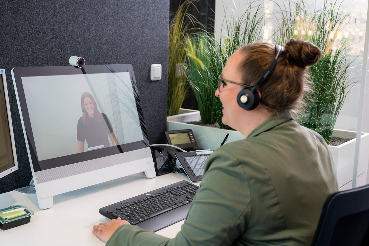 Junge Frau ist in einer digitalen Beratung und lächelt in Richtung der Kundin.