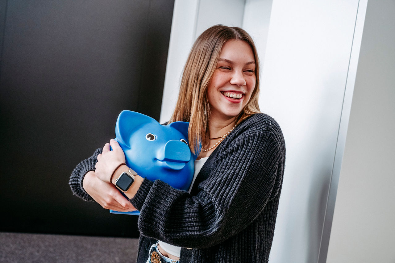 Junge Frau lächelt und hält ein blaues Sparschwein in der Hand