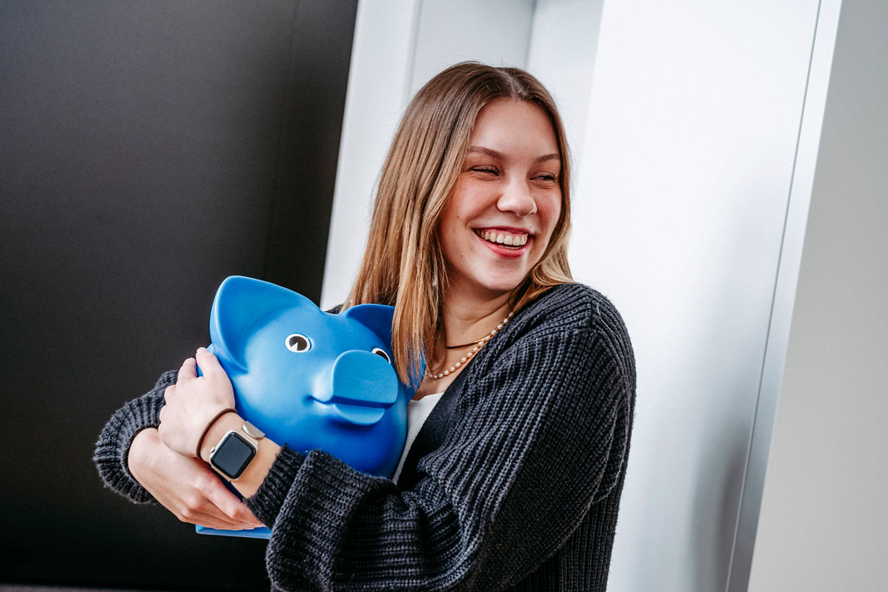 Junge Frau lächelt und hält ein blaues Sparschwein in der Hand