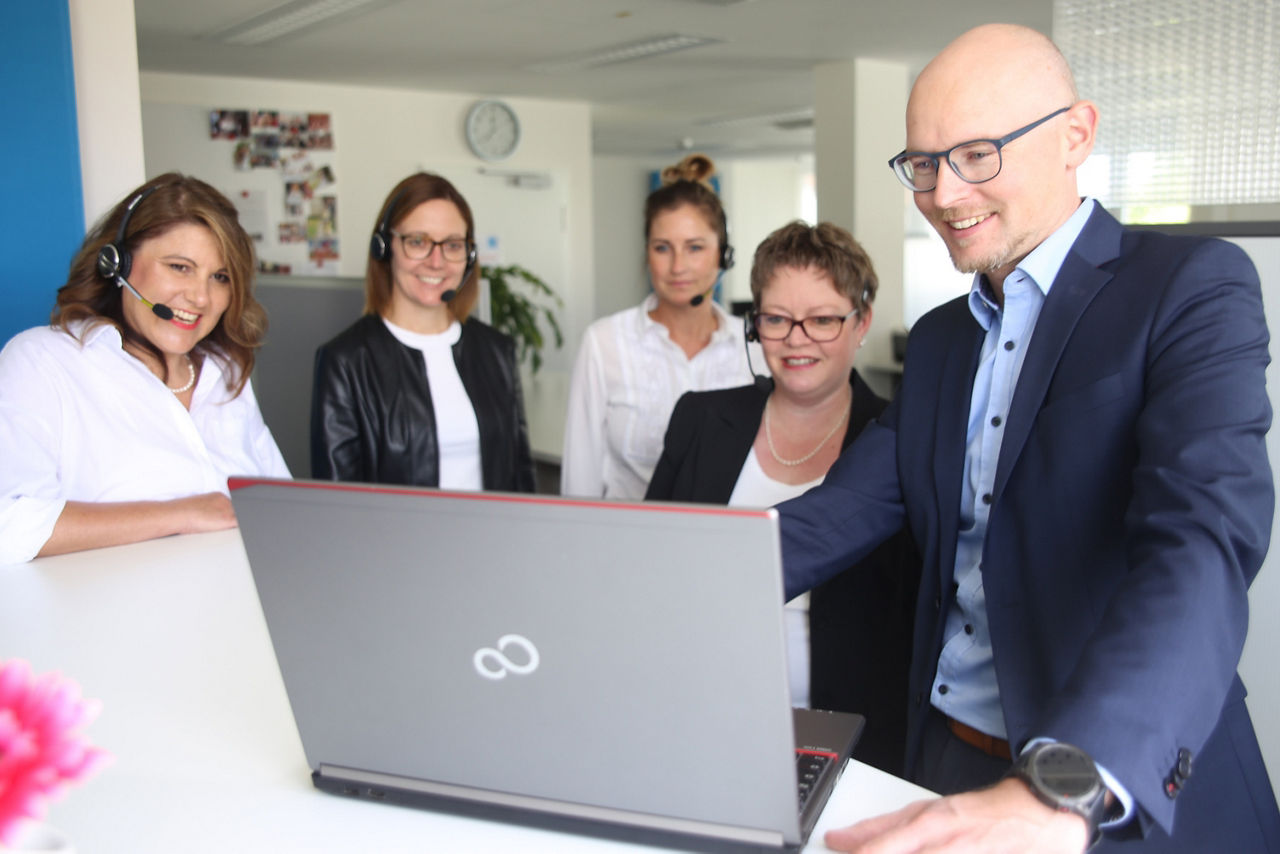 Mehrere Mitarbeiter des KundenServiceCenters schauen auf einen Laptop