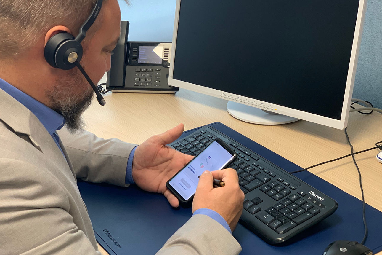 Mitarbeiter mit Headset und Online-Banking am Smartphone