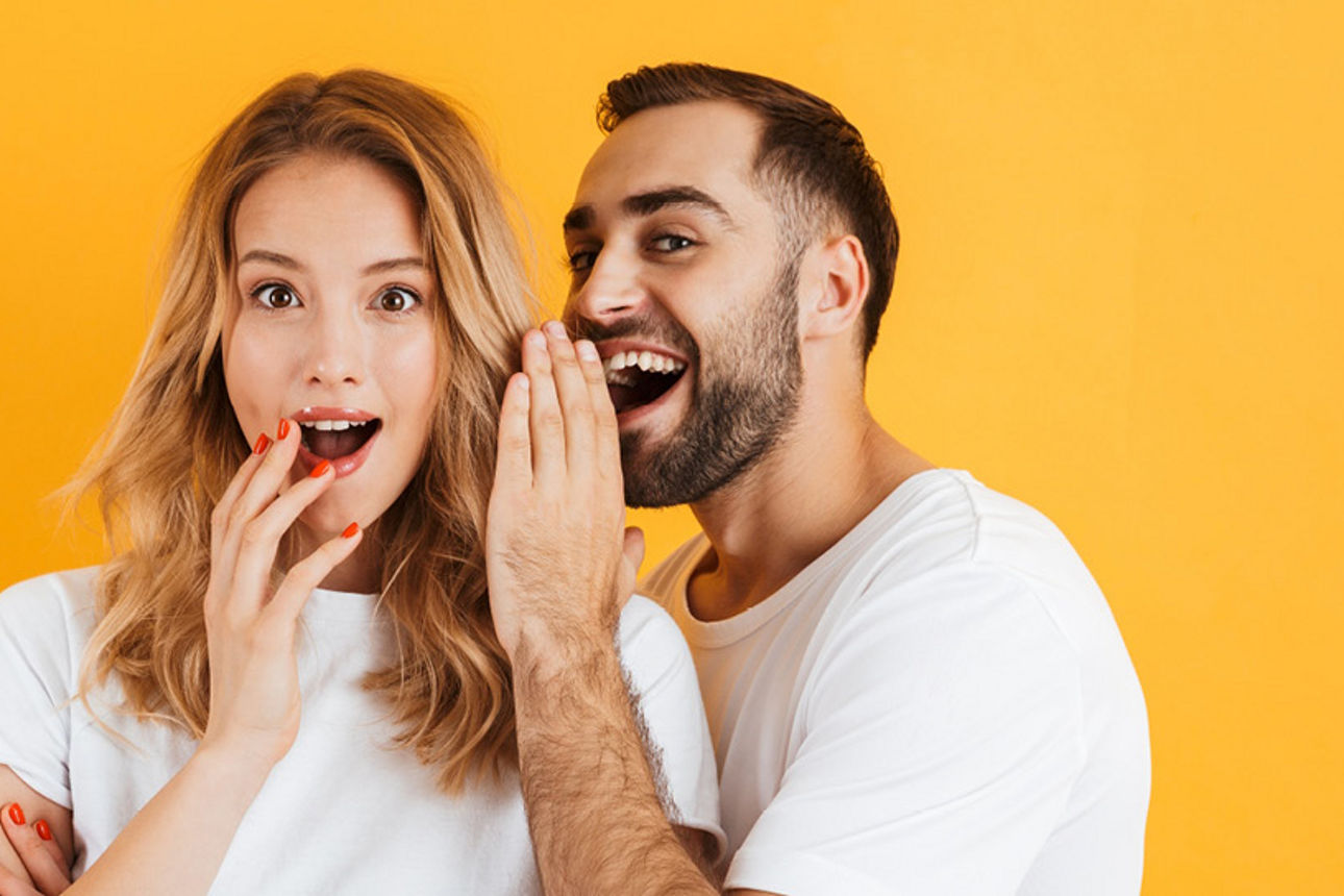 Frau ist erstaunt. Daneben ein amnn der ihr etwas ins Ohr flüstert