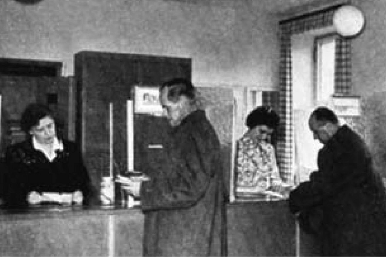 ein altes Bild in Schwarz-Weiß, mehrere Menschen stehen vor einem Bankschalter