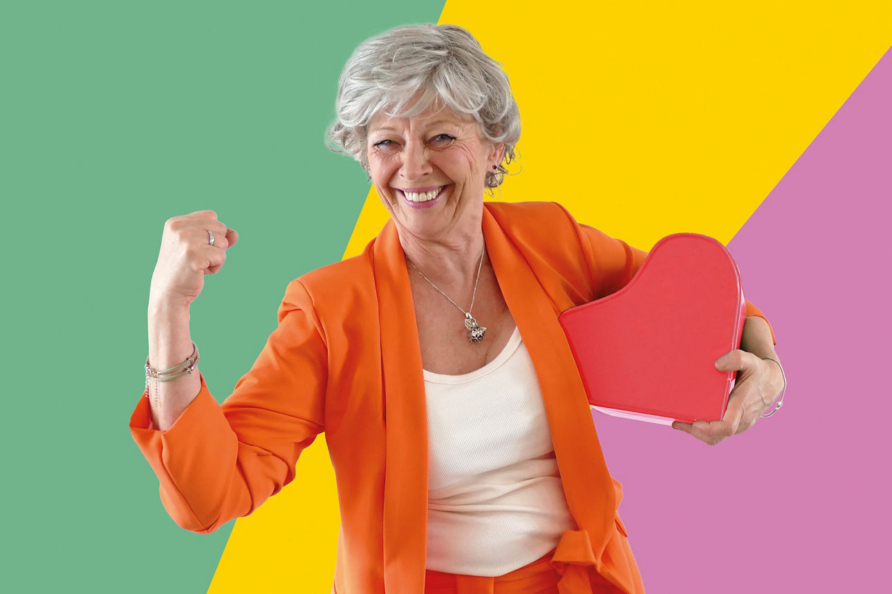 Käthe steht vor einem grün, gelb und rosa gestreiften Hintergrund und posiert mit vor der Kamera. 