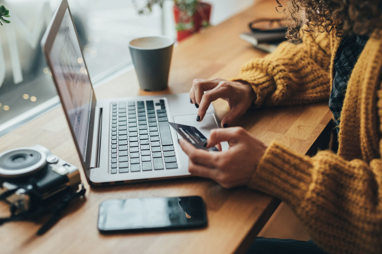 Frau sitzt in einem Cafe mit Laptop, Handy und Karte